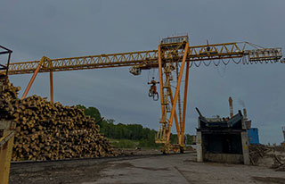 Portal crane with wire rope hoist and claw used to pick up logs at a paper mill.