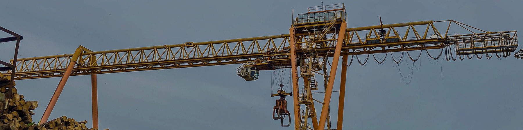 Portal crane with wire rope hoist and claw used to pick up logs at a paper mill.